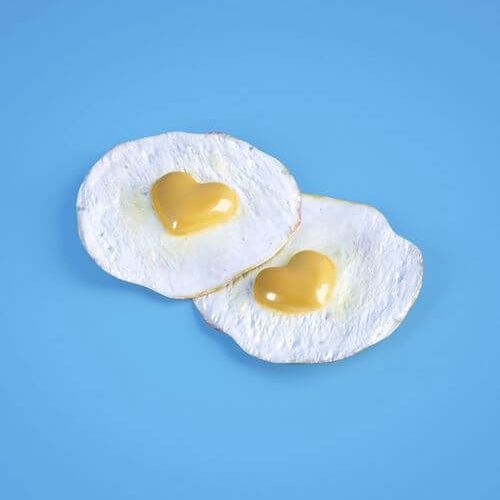 Photo à fond bleu ciel représentant deux oeufs sur le plat dont les jaunes représentent des coeurs